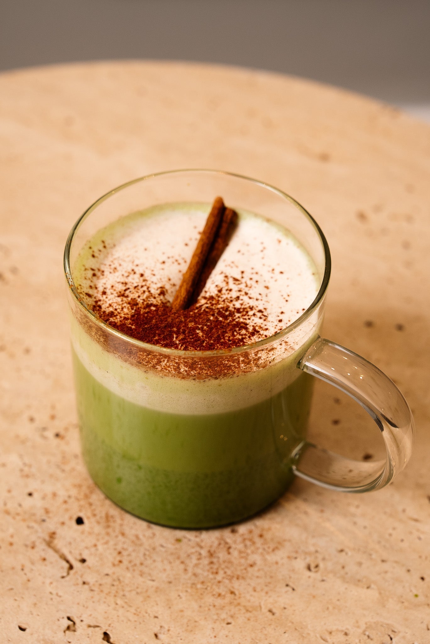 Ceremonial grade matcha latte with foam, cinnamon stick and powder in a clear glass mug