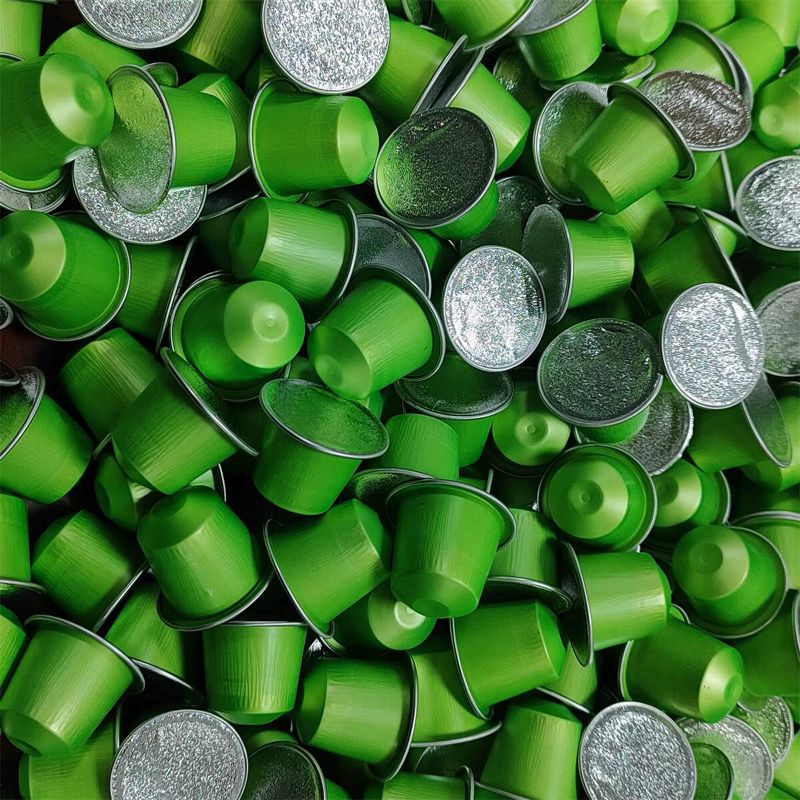 Pile of green matcha tea capsules with silver tops for single-serve brewing