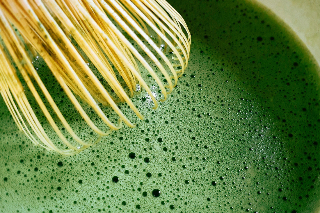 Close-up of bamboo whisk mixing frothy ceremonial grade matcha tea